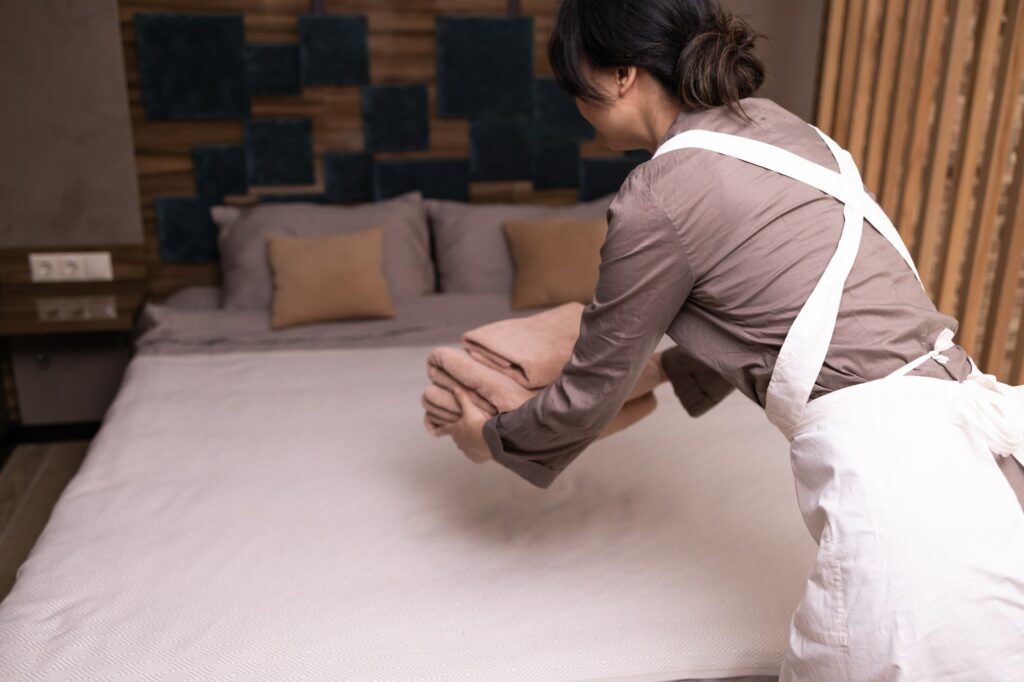 Asian female maid puts fresh towels on bed in hotel room