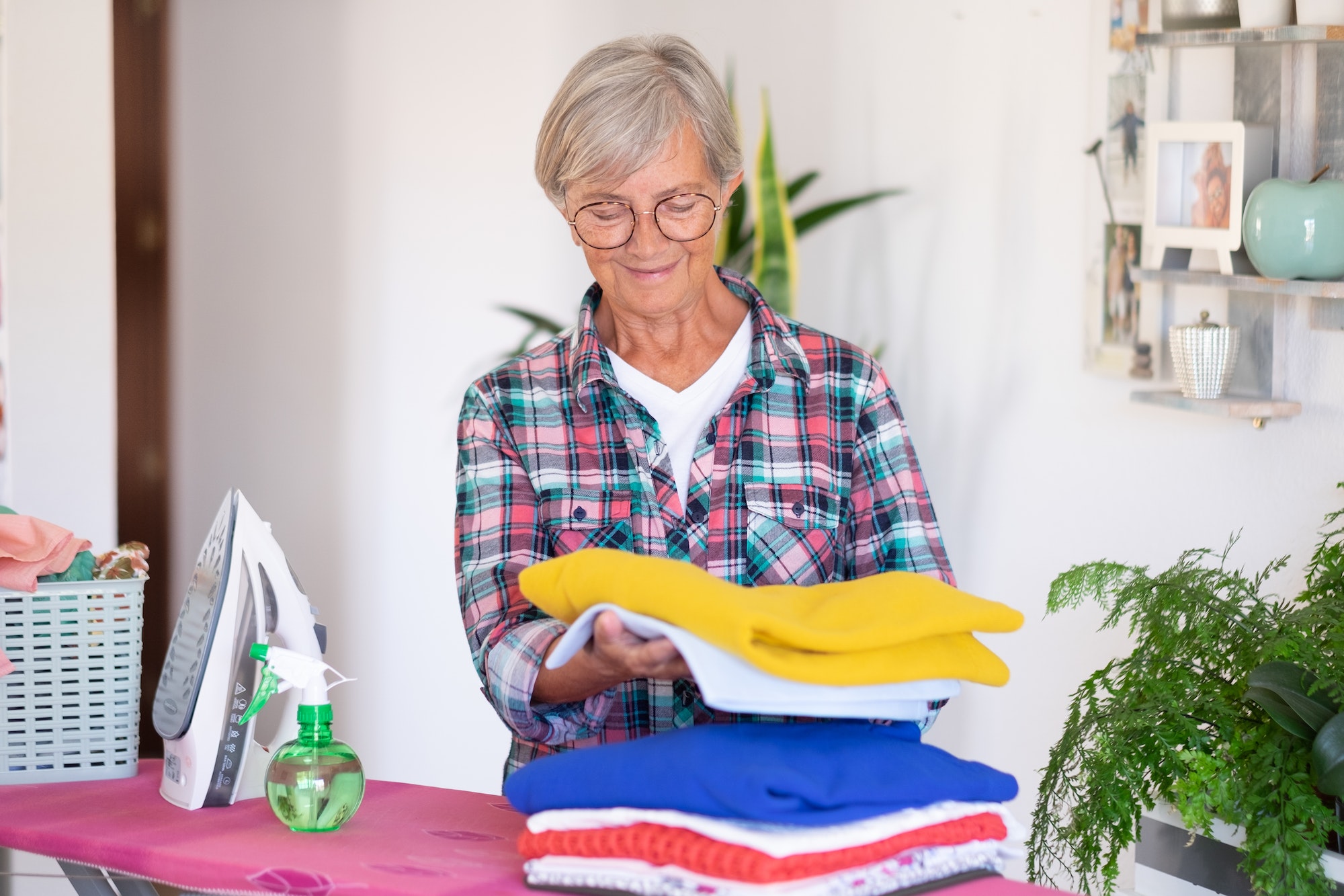 Caucasian smiling senior woman ironing clothes at home on ironing board
